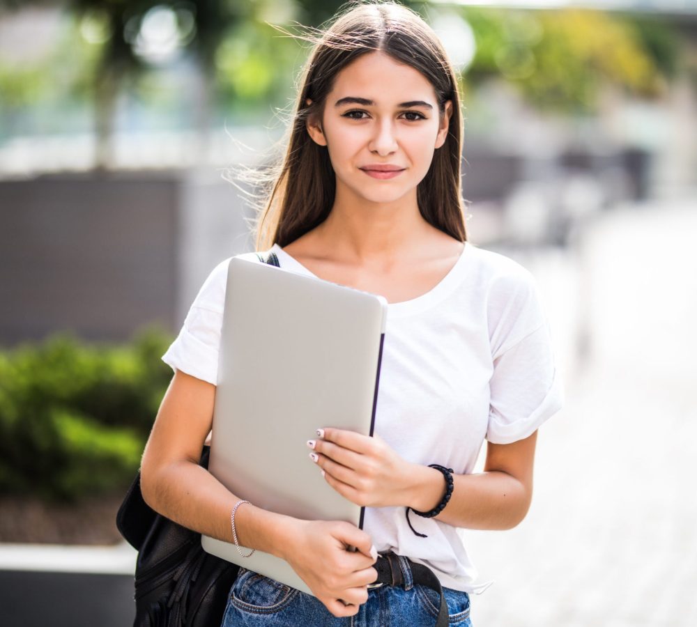 Portrait of young happy blogger with modern laptop near stone wall